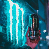 Hand holding up a Monster Energy Drink infront of blue glowing "M."