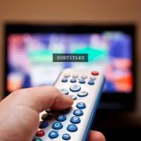 TV remote in front of blurry TV with "subtitles" written.
