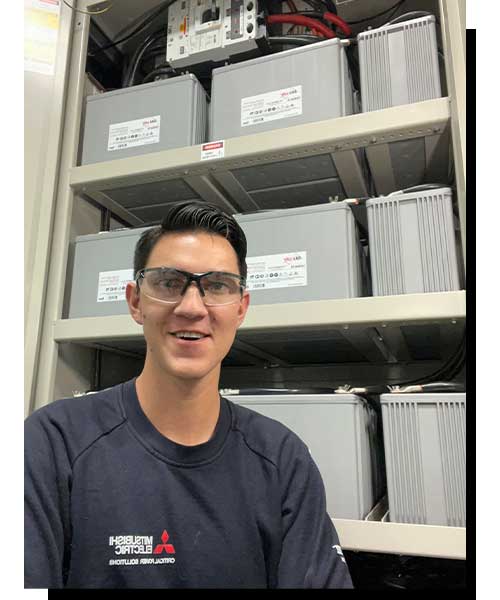Field Technician smiling on site in front of batteries.